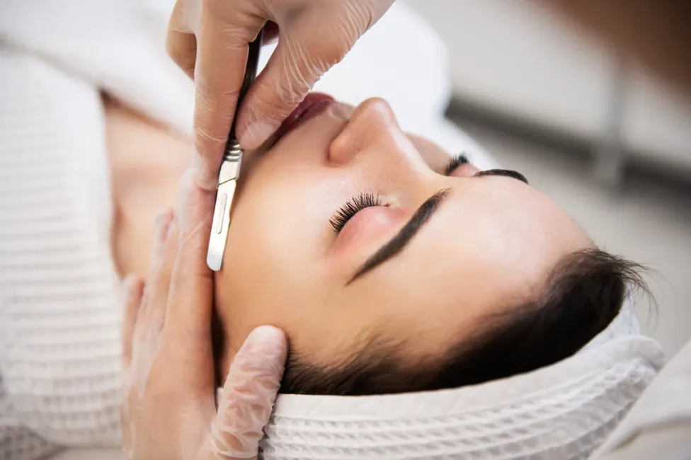 Dermaplaning treatment exfoliating a client’s cheek with a surgical blade at Skincredible Wichita
